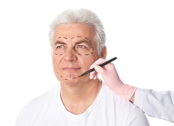 Photo of Doctor drawing marks on mature man's face for cosmetic surgery operation against white background