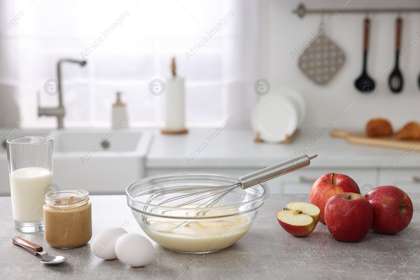 Photo of Whisk, bowl, beaten eggs and other ingredients on grey table indoors, space for text