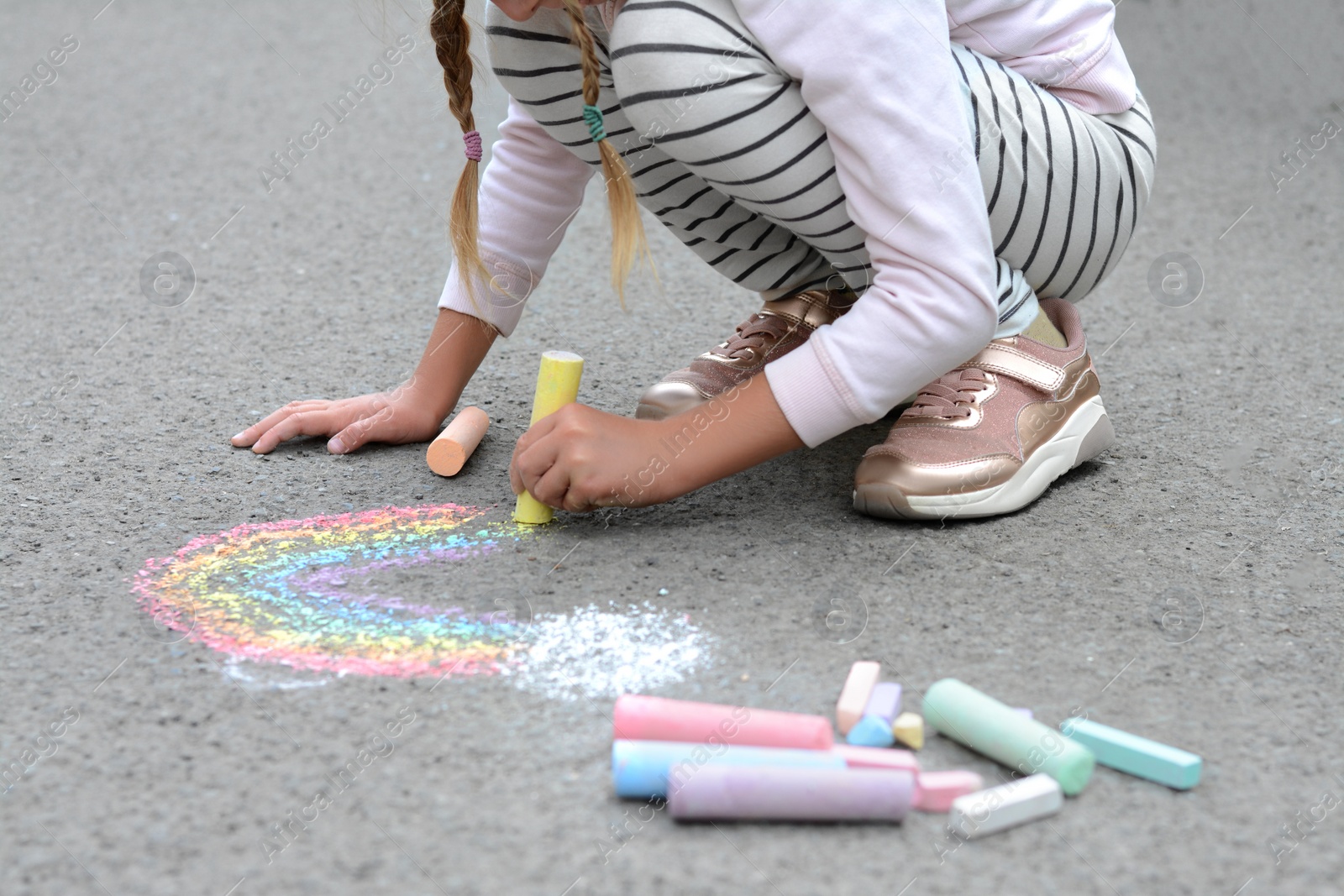 Photo of Little child drawing rainbow with chalk on asphalt, closeup