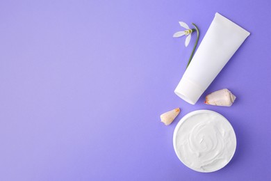 Photo of Jar and tube of cream, seashells with snowdrop flower on violet background, flat lay. Space for text