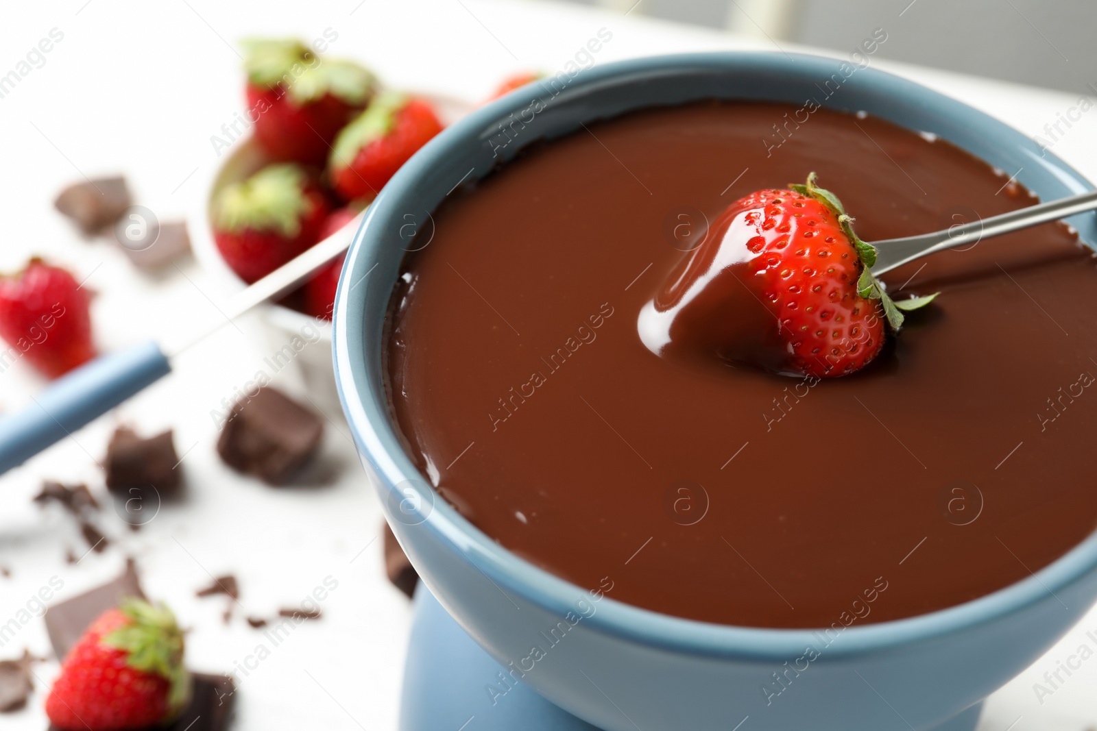 Photo of Dipping strawberry into fondue pot with chocolate, closeup