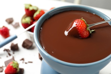 Photo of Dipping strawberry into fondue pot with chocolate, closeup