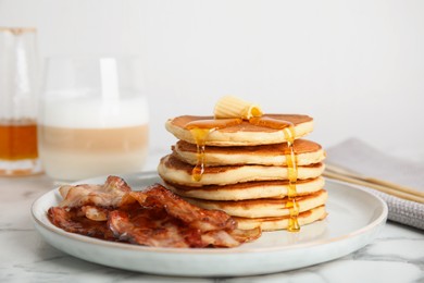 Delicious pancakes with maple syrup, butter and fried bacon on white marble table