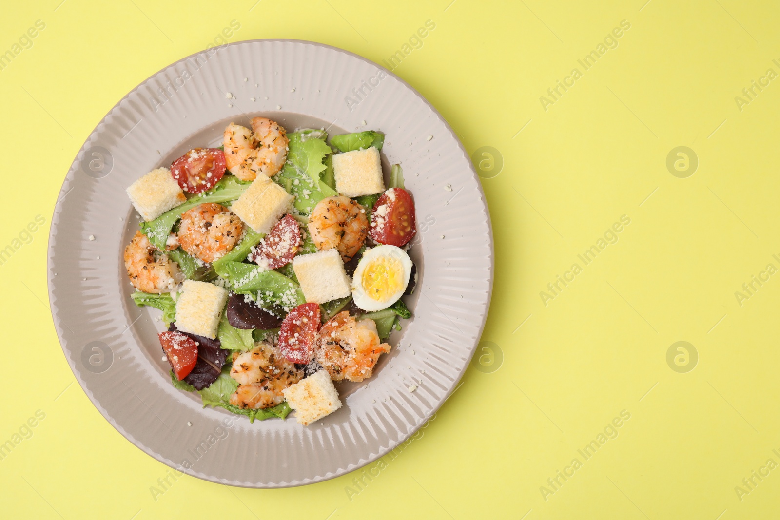 Photo of Delicious Caesar salad with shrimps on yellow background, top view. Space for text