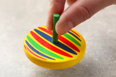 Woman playing with bright spinning top at grey textured background, closeup