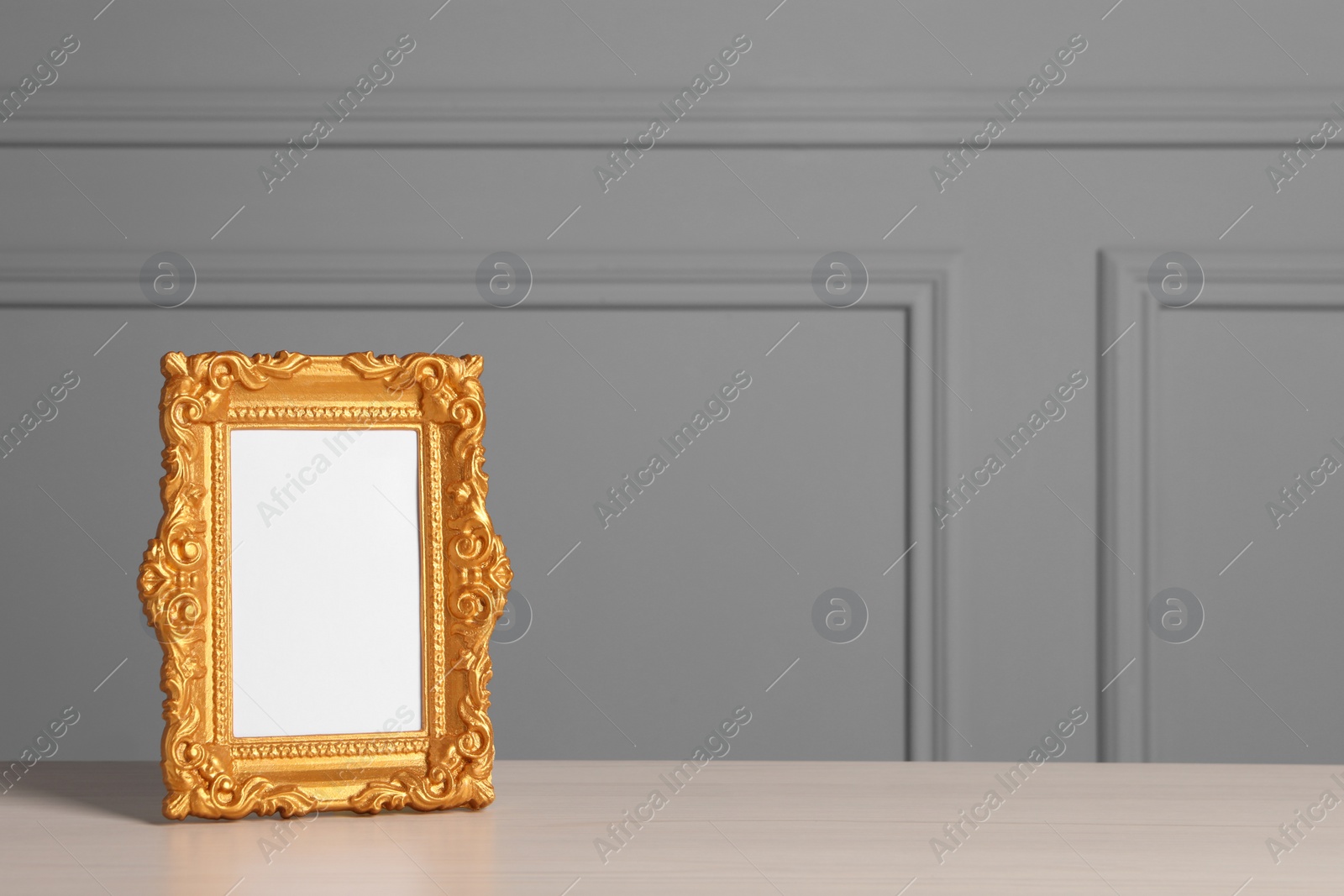 Photo of Beautiful golden vintage frame on white wooden table near grey wall, space for text