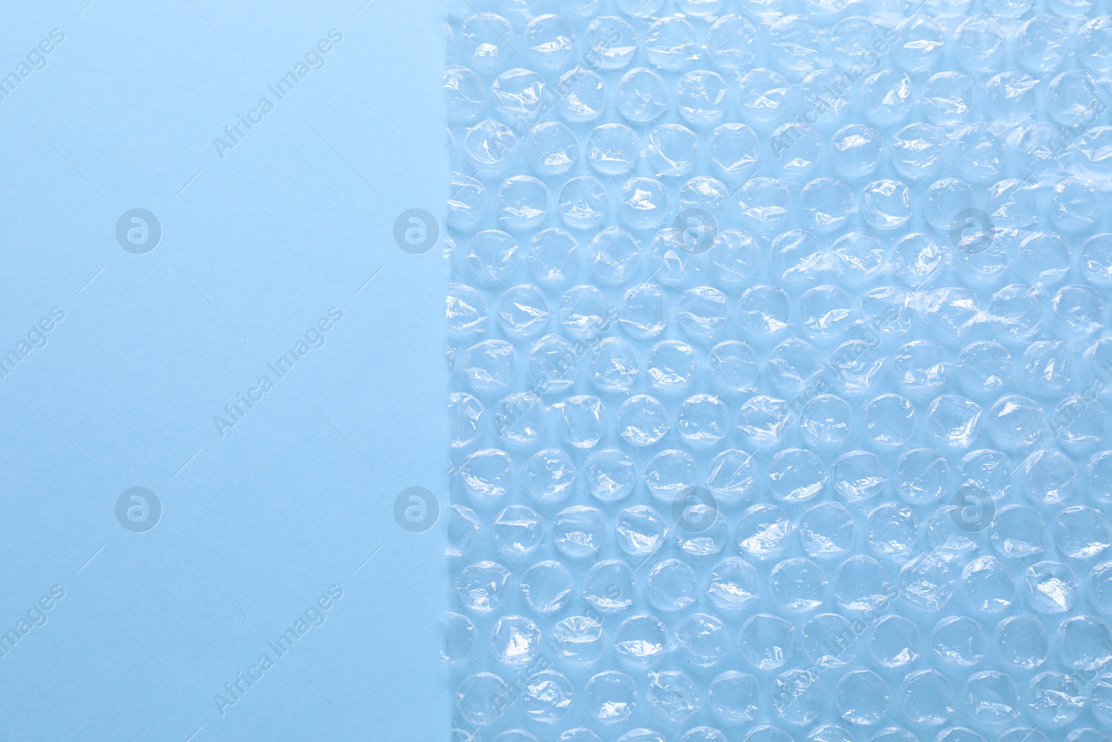 Photo of Transparent bubble wrap on light blue background, top view. Space for text