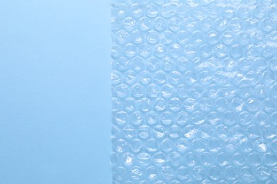 Transparent bubble wrap on light blue background, top view. Space for text