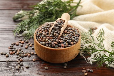Raw lentils in bowl and dill on wooden table, closeup