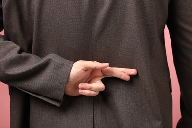 Man crossing his fingers on pink background, closeup and back view
