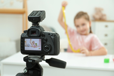 Photo of Cute little blogger with slime recording video at home, focus on camera