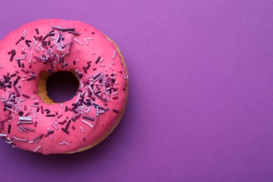Sweet glazed donut decorated with sprinkles on purple background, top view and space for text. Tasty confectionery