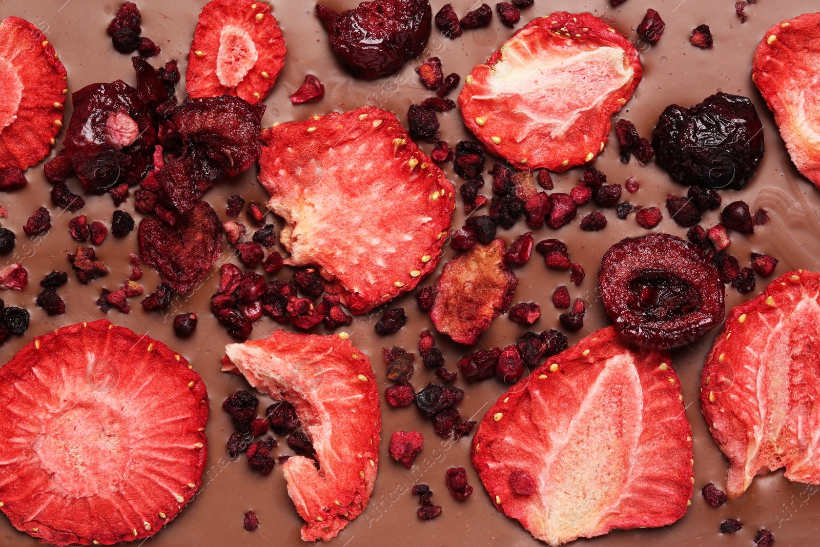 Photo of Chocolate bar with freeze dried strawberries and cherries as background, closeup