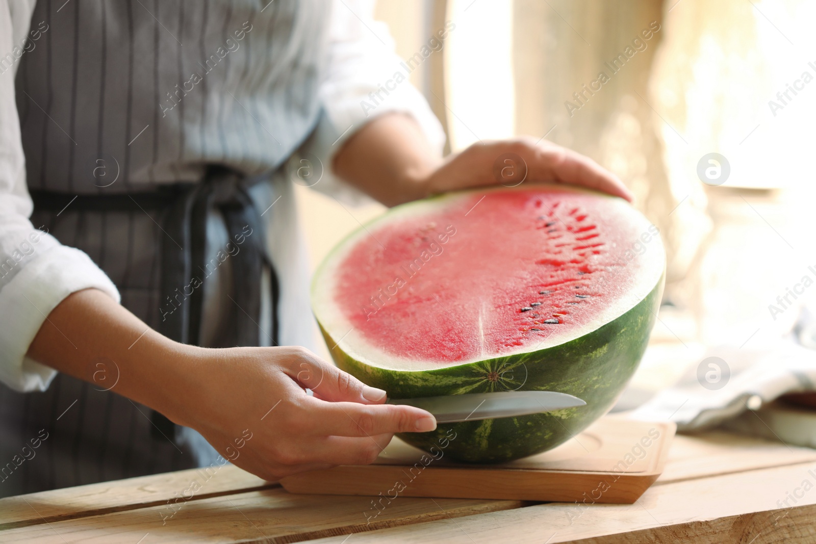 Photo of Woman cutting fresh juicy watermelon at wooden table, closeup