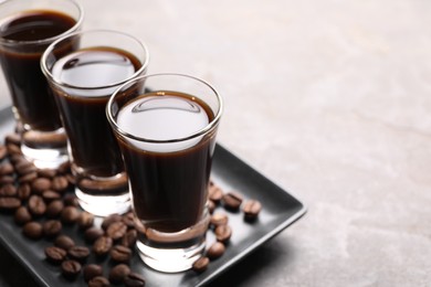 Photo of Shot glasses with coffee liqueur and beans on light grey table, closeup. Space for text