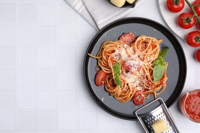 Tasty pasta with tomato sauce, cheese and basil served on white tiled table, flat lay. Space for text