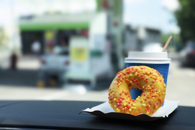 Photo of Paper coffee cup and doughnut on car dashboard at gas station
