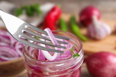 Fork with slice of pickled onion over jar on table, closeup