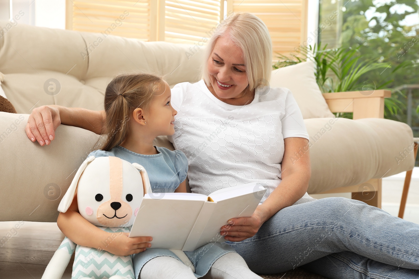 Photo of Happy grandmother with her granddaughter reading book together at home