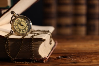 Pocket clock with chain and book on wooden table, closeup. Space for text