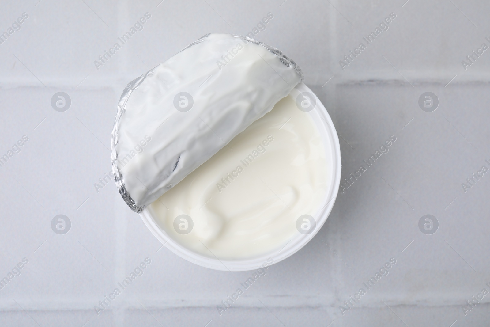 Photo of Delicious natural yogurt in plastic cup on white tiled table, top view