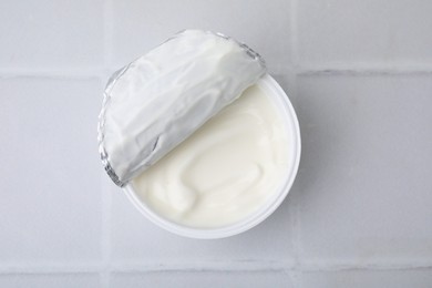 Delicious natural yogurt in plastic cup on white tiled table, top view