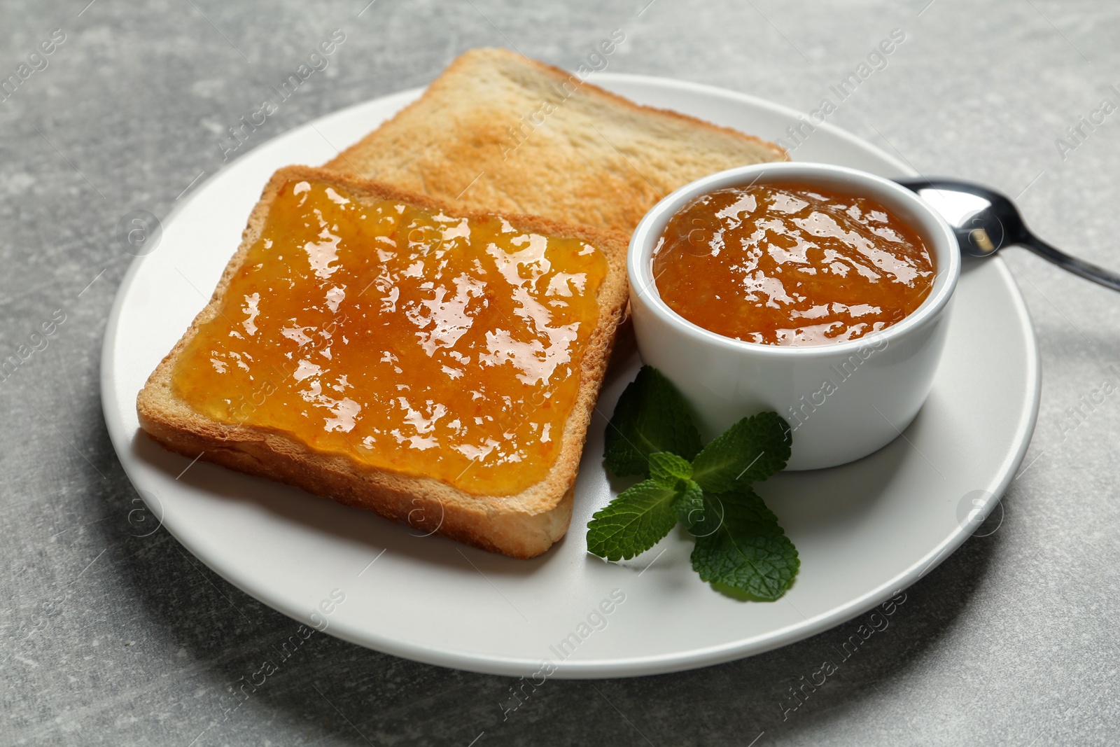 Photo of Delicious toasts served with jam and mint on light grey table, closeup