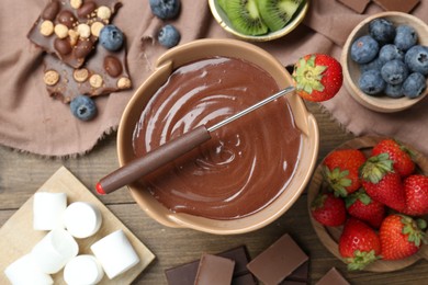 Photo of Fondue pot with melted chocolate, marshmallows, fresh kiwi, different berries and fork on wooden table, flat lay