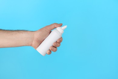 Photo of Man holding nasal spray on light blue background, closeup. Space for text