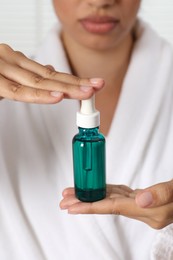 Woman with bottle of cosmetic serum on light background, closeup