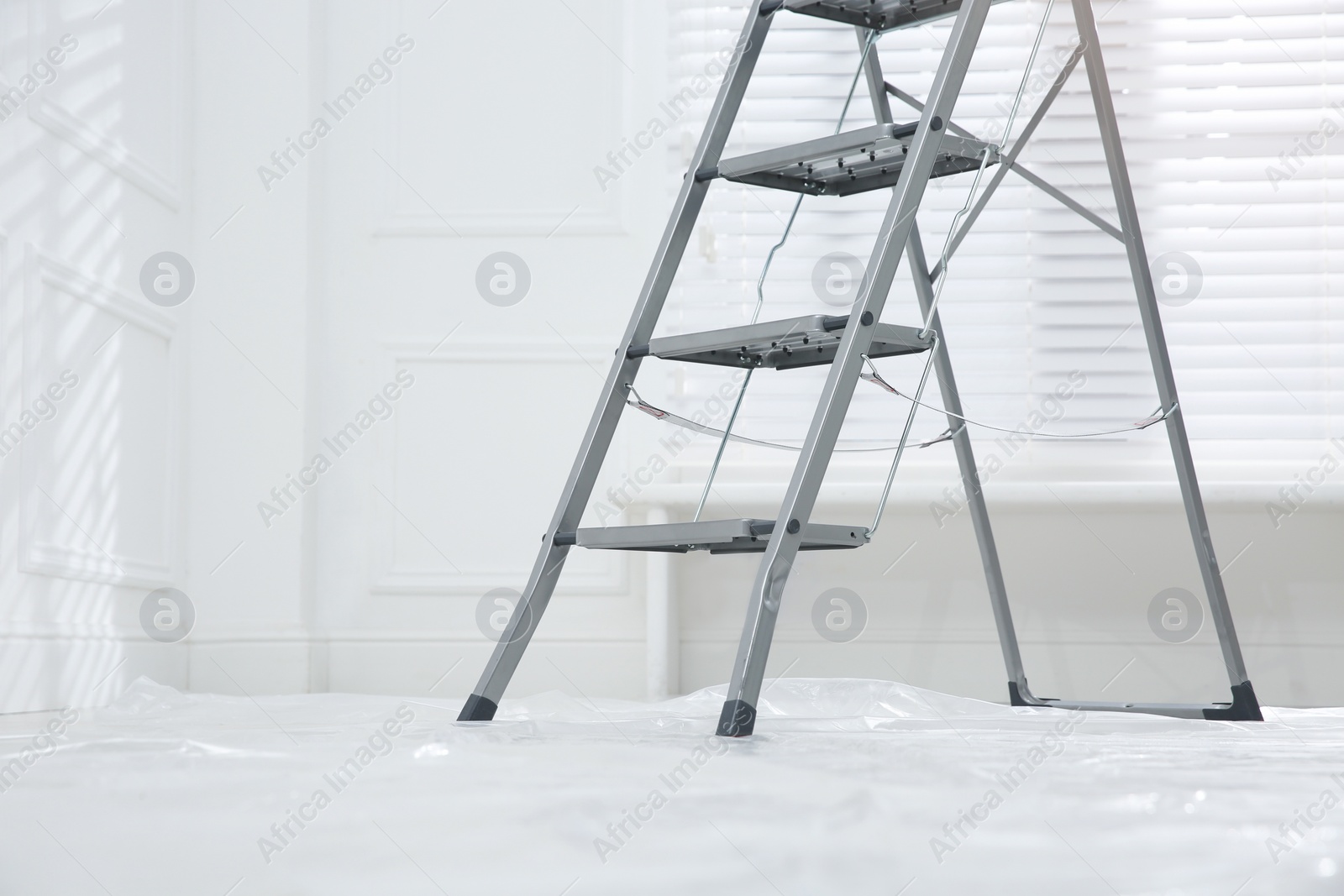 Photo of Metal stepladder on floor covered with plastic in empty room, space for text