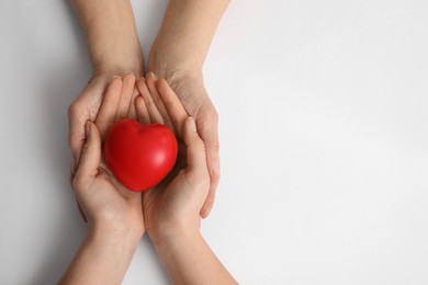 Photo of Young and elderly women holding red heart on white background, top view