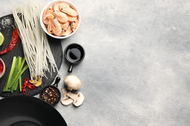 Flat lay composition with black wok, spices and products on grey textured table. Space for text