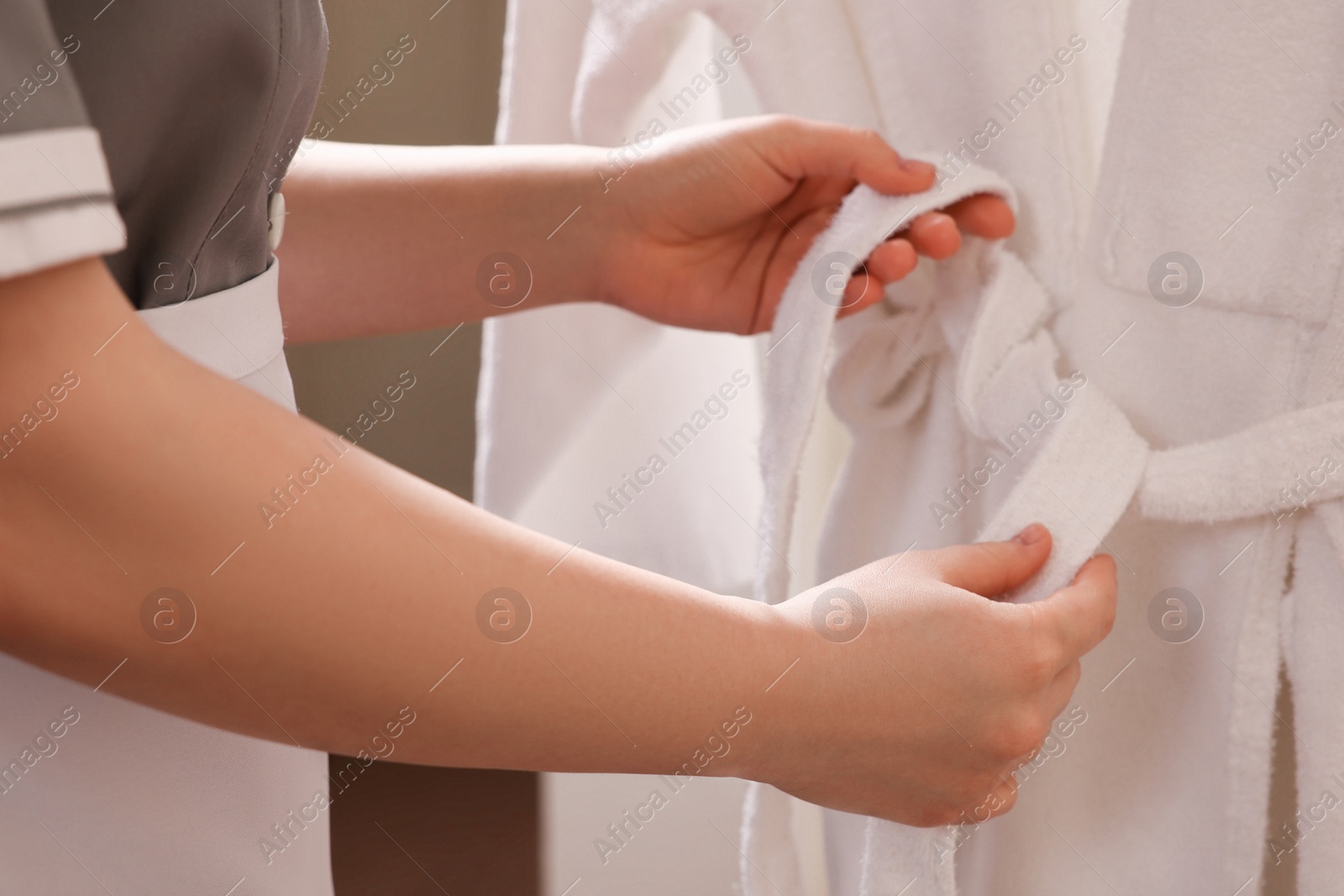 Photo of Young chambermaid tying belt on bathrobe in hotel room, closeup