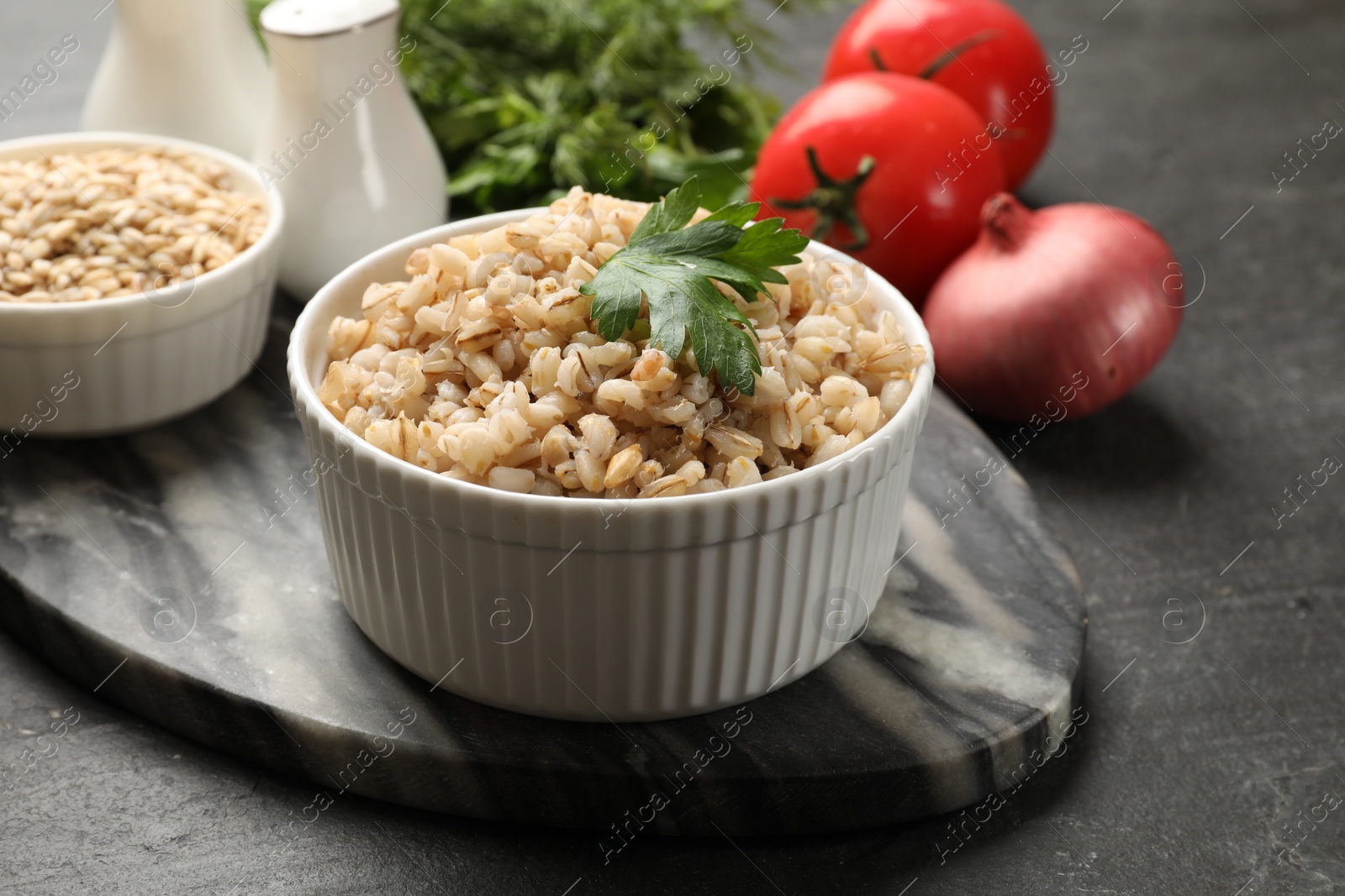 Photo of Tasty pearl barley porridge and parsley in bowl on dark textured table, closeup