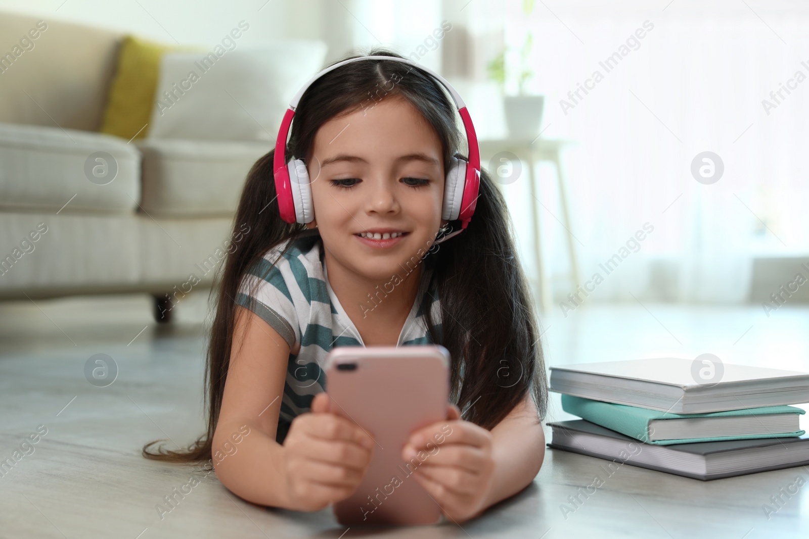 Photo of Cute little girl with headphones and smartphone listening to audiobook at home