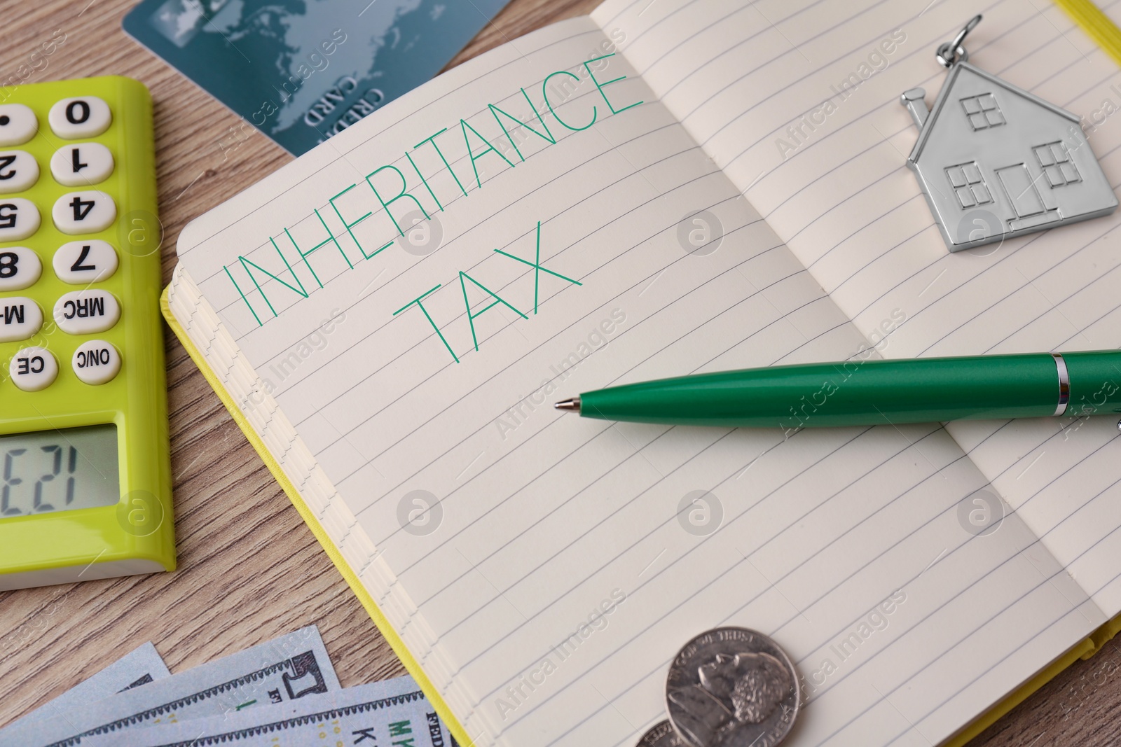 Photo of Notepad with phrase Inheritance Tax, house shaped key chain, money and calculator on wooden table, closeup