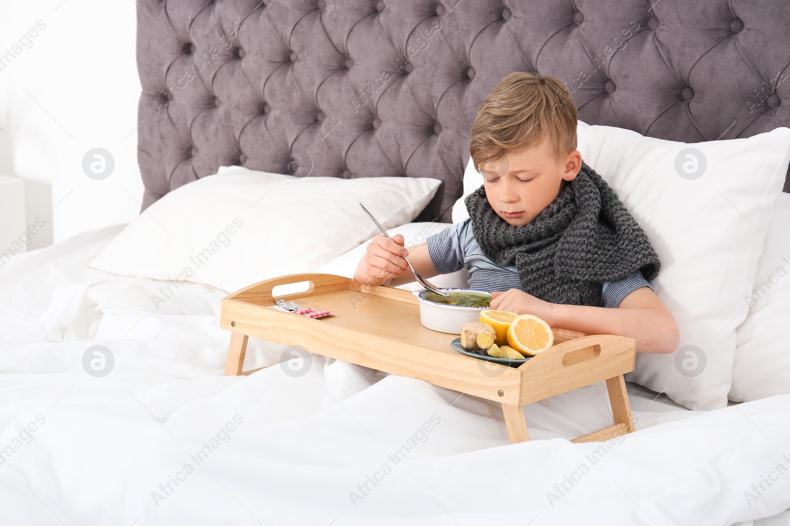 Photo of Sick little boy eating broth to cure cold in bed at home