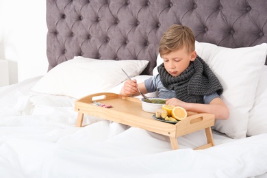 Photo of Sick little boy eating broth to cure cold in bed at home