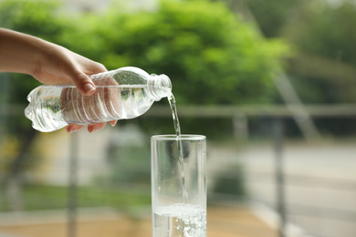 Photo of Woman pouring water from bottle into glass against blurred background, closeup