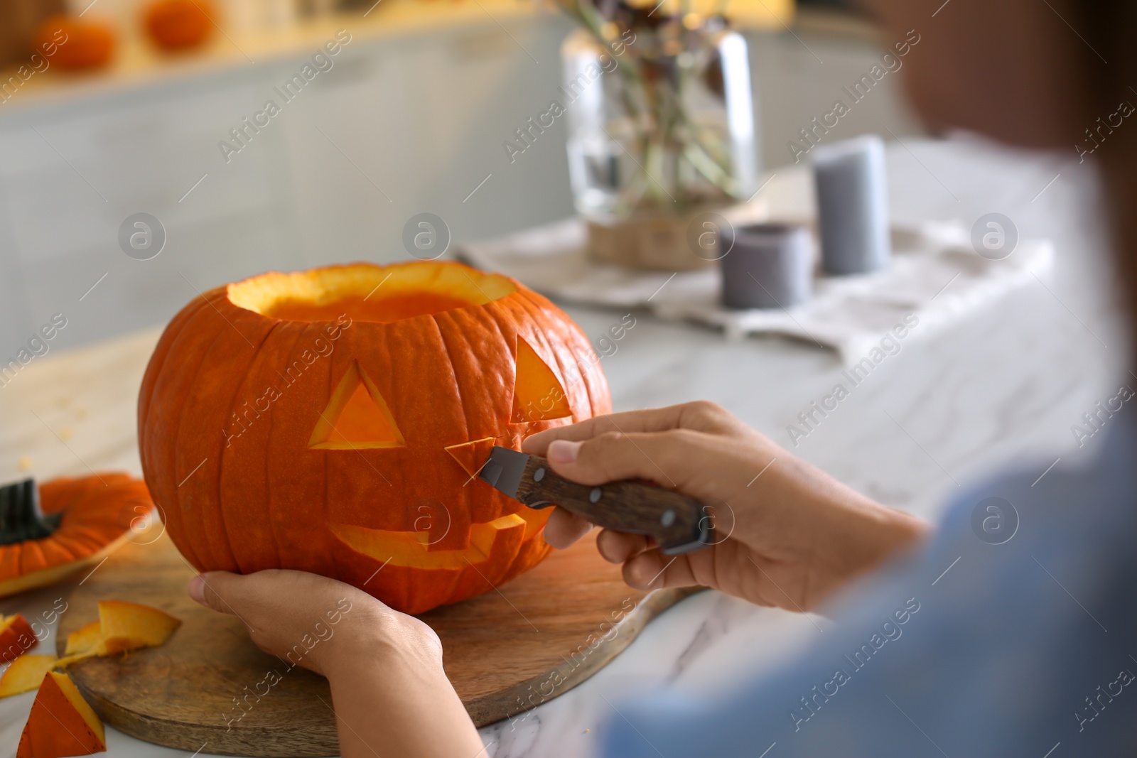 Photo of Woman making pumpkin jack o'lantern at table in kitchen, closeup. Halloween celebration