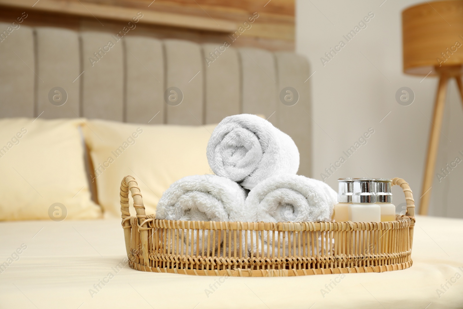 Photo of Rolled clean towels and shampoo bottles on bed indoors
