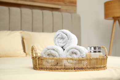 Photo of Rolled clean towels and shampoo bottles on bed indoors