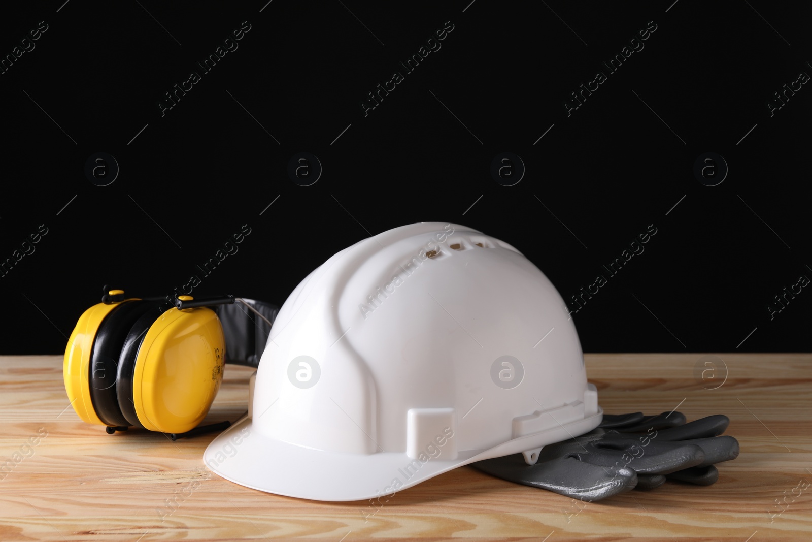 Photo of Hard hat, earmuffs and gloves on wooden table, space for text. Safety equipment