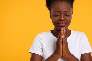 Woman with clasped hands praying to God on orange background. Space for text