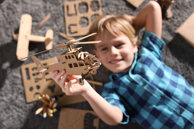 Photo of Little boy playing with cardboard helicopter on floor at home, top view. Creative hobby