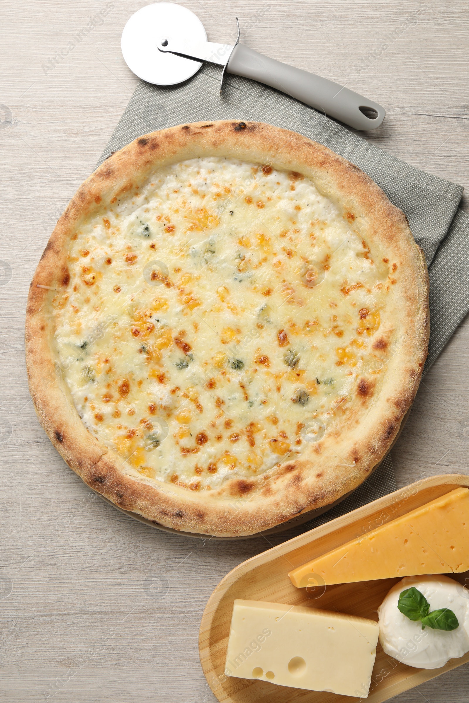 Photo of Delicious cheese pizza, cutter and different kinds of cheese on wooden table, flat lay