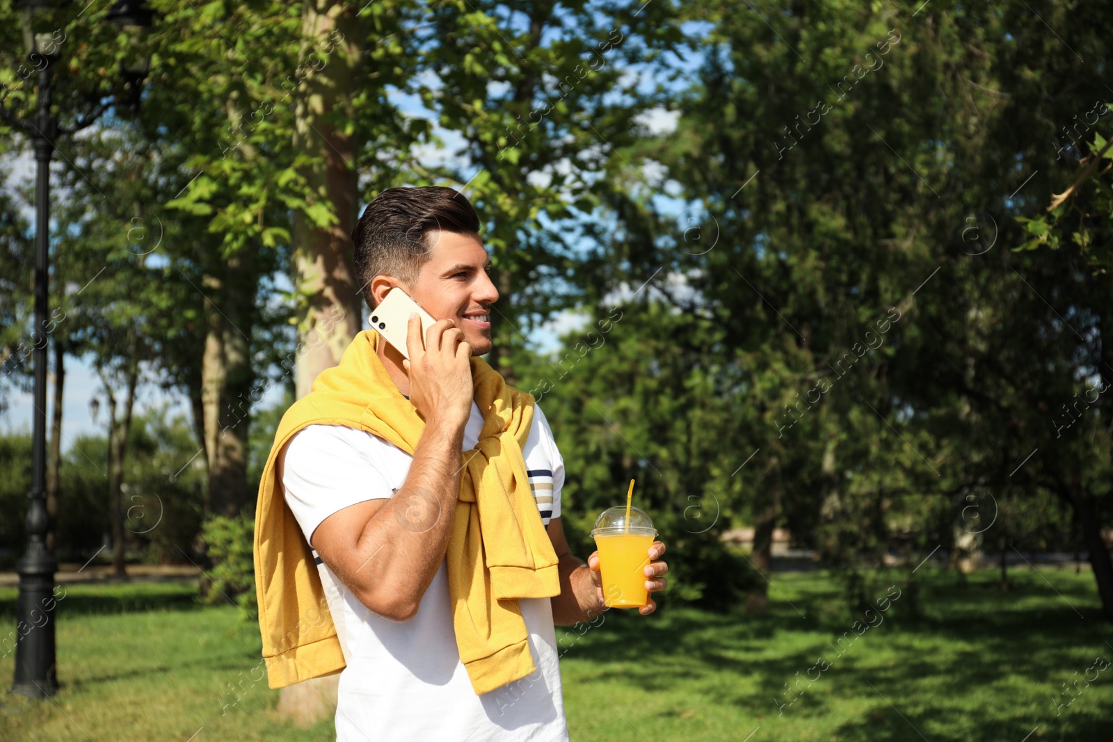 Photo of Handsome man with refreshing drink talking on smartphone in park