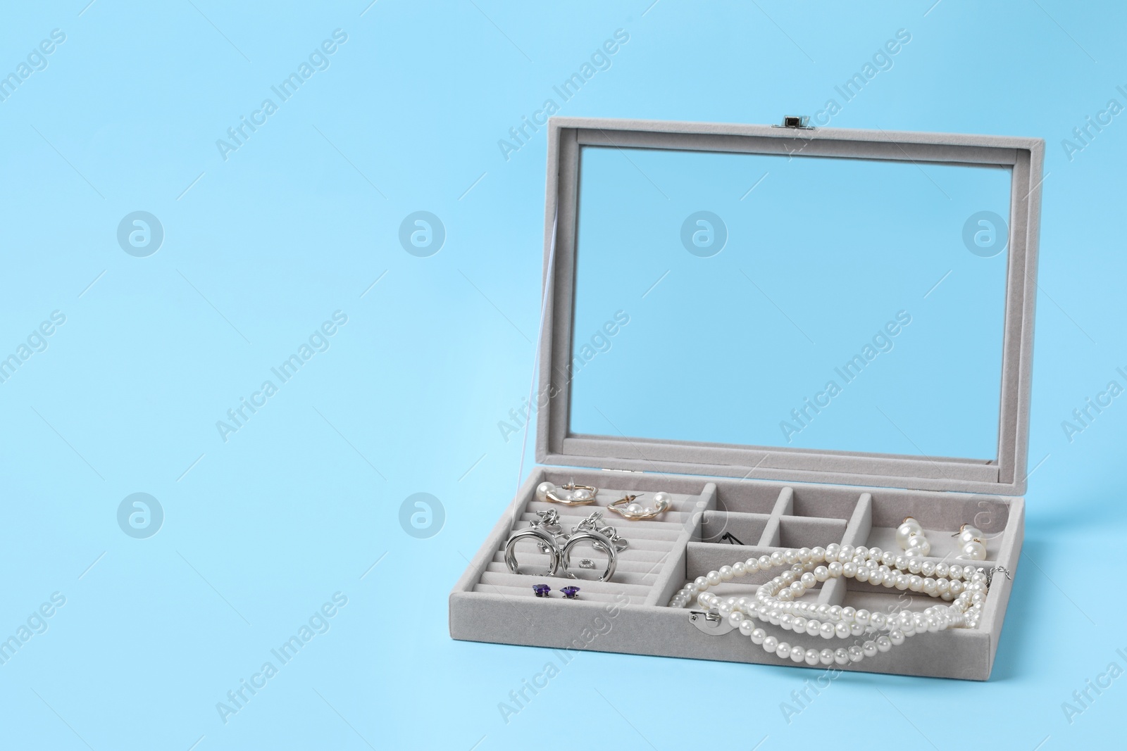 Photo of Jewelry box with many different accessories on light blue background, space for text