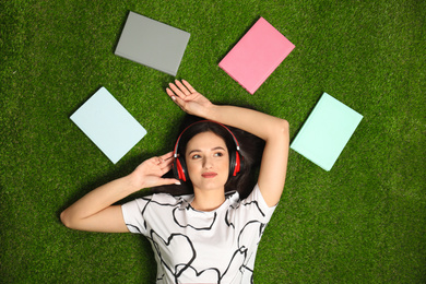 Young woman listening to audiobook while lying on grass, flat lay